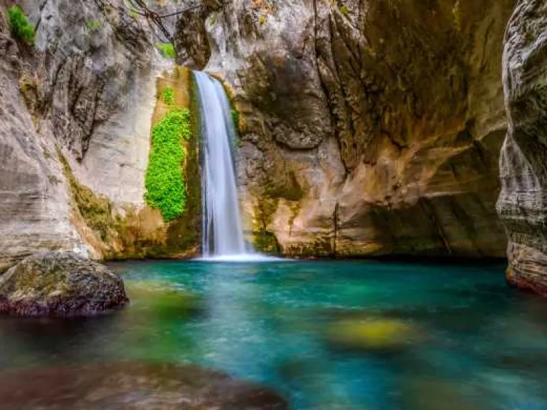 O cascadă peste stâncă acoperită de mușchi, într-un bazin verde din canionul Sapadere