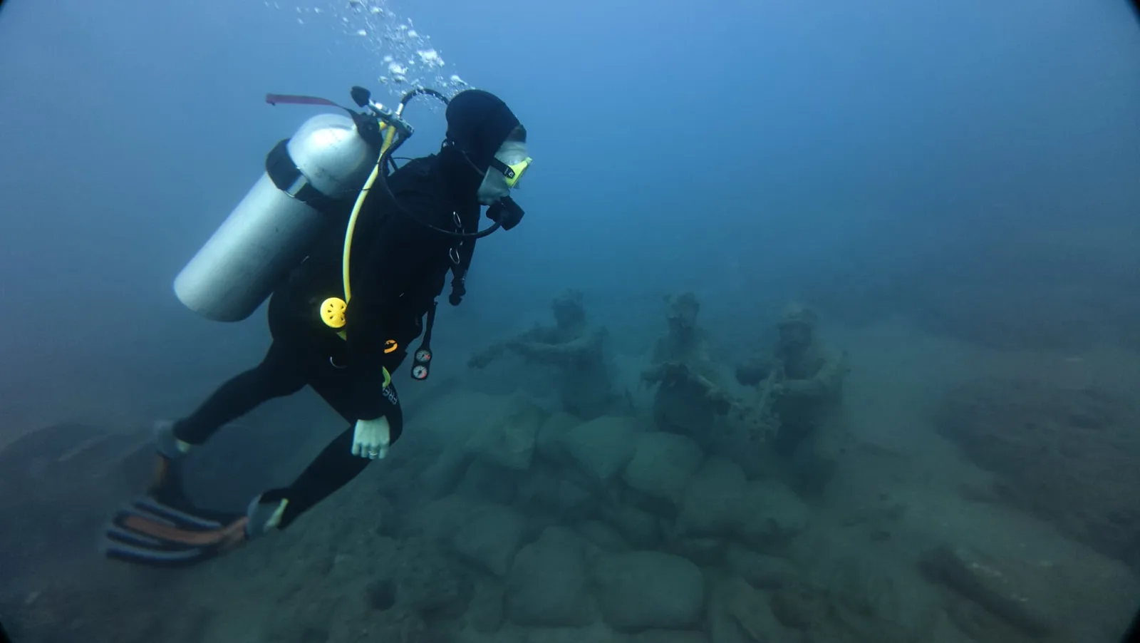 diver swimming over statues side
