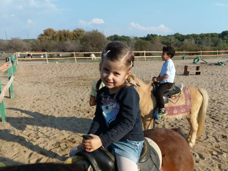 Zwei Kinder auf Ponys in einem Sandpaddock mit Holzzaun